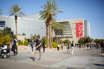 people with backpacks walking past a large building. The building has a red "UNLV" banner prominently displayed.
