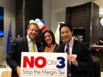 Three individuals holding "No on 3: Stop the Margin Tax" sign