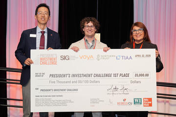 Three people holding an oversized ceremonial for $5,000 made out to "President's Investment Challenge First Place"