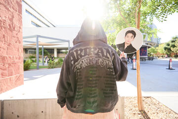 individual wearing a BTS Arirang tour hoodie and holding a Jungkook fan with sun above