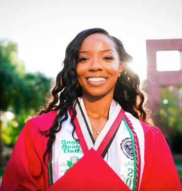 A portrait of Sayla Daily in a red cap and gown.