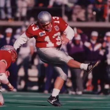 UNLV football player wearing a red No. 13 jersey, silver helmet and silver pants swings his right leg after kicking a football during a game