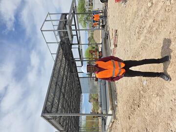 student in front of steel beams wearing a construction jacket and a hard hat