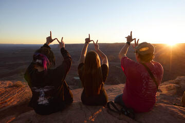 three students looking over canyon at sunset making "LV" symbol with hands