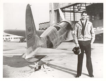 Howard Hughes stands next to a plane in black and white photo