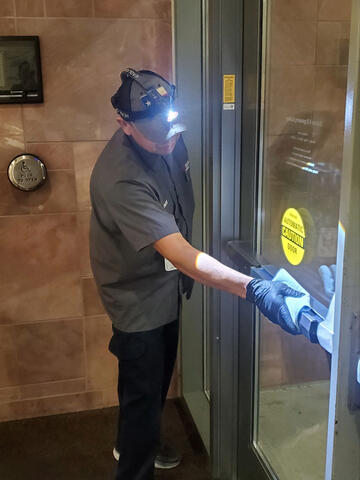 Hector Mariche, a custodial worker at UNLV, cleans a building door with a headlamp on his hat.