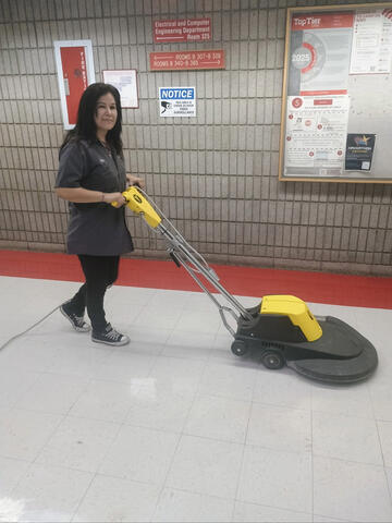 A woman pushes a high speed burnisher along a floor.