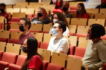 Students wearing face covering sit socially distanced in a classroom auditorium