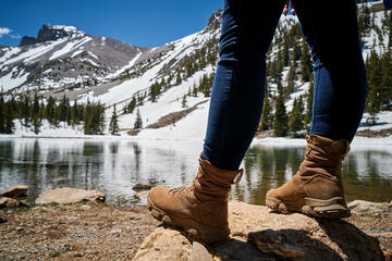 closeup of a person's hiking boots at edge of mountain lake