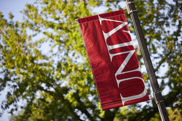 Red UNLV pole banner amidst foliage