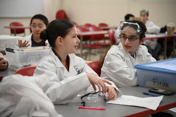 Two young students in lab coats during classroom discussion