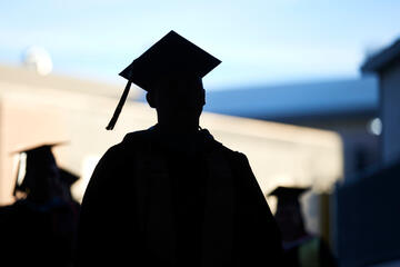 A silhoutte of a student wearing a cap and gown with the tassel swaying as they walk