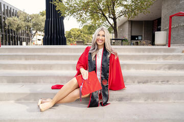 female student poses on steps in red graduation gown