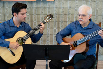 two men sitting and playing acoustic guitars