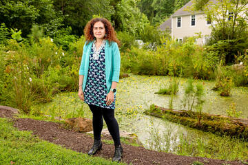 woman standing outside in front of pond and bushes