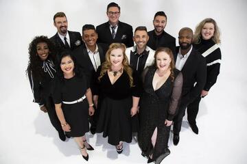 eleven members of an a cappella group dressed in black in front of white background