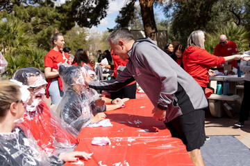 fundraising event where one woman sitting at a table is hit by a pie