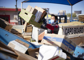 man wearing masks organizes piles of cardboard for recycling