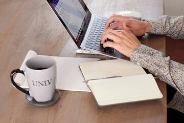 man's hands shown typing on laptop with UNLV branded coffee mug on table