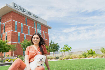 Jennifer Chen, MD, and her dog Archibald sitting on the lawn of the Kirk Kerkorian Medical Education Building.
