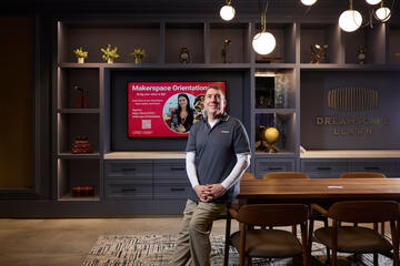 man leaning against table in front of TV screen and wall that reads Dreamscape Learn