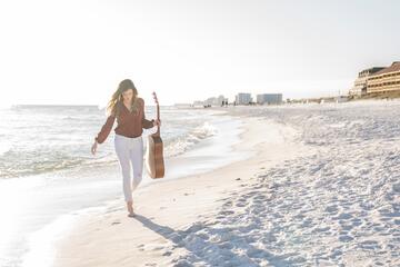 woman holding guitar while walking on the shore