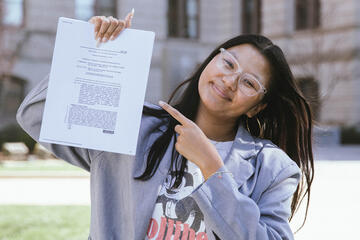woman posing outside holding up a legal document and pointing to it