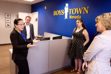 Ying Guo discussing with colleagues in front of wall with Boys Town logo