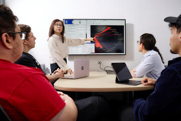 female instructor leads student discussion using screen showing cybersecurity graphics