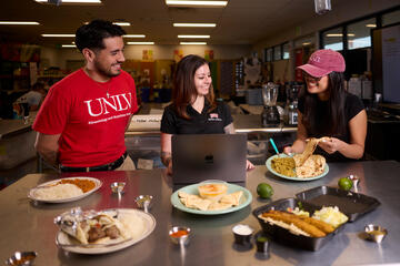 man and two women look over array of cultural cusines on tabletop