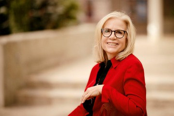 Susan Adair wearing red sweater and glasses while sitting on steps