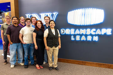 A group of students and faculty stand next to the Dreamscape Learn signage in the Lied Library