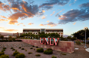 UNLV sign in foreground of four story building with clouds above