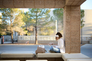 student sitting on bench using laptop
