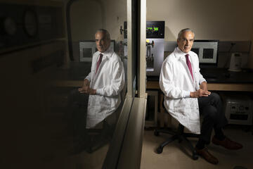 Dr. Jeffrey Cummings is pictured in a white lab coat in his lab, with his image reflected in a mirror