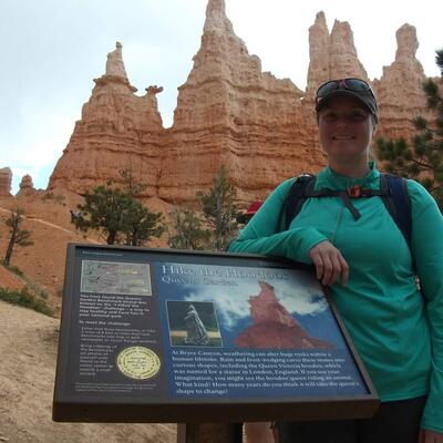 A woman leaning against a sign for "Hike the Hoodoos"
