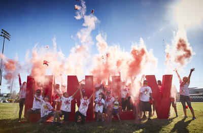Photo of UNLV students and youth standing by large, red &quot;UNLV&quot; letters with red smoke rising around them