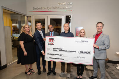 Six people pose for a group photo holding a huge check