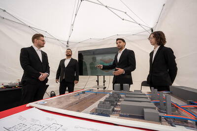 Four UNLV Engineering students stand in front of a TV screen as they present their project at Senior Design