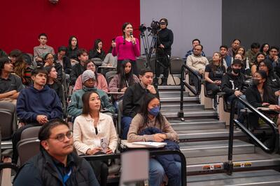 A student stands up amid a large audience crowd to offer her startup idea