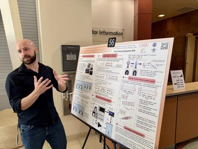 A student gestures toward his research poster