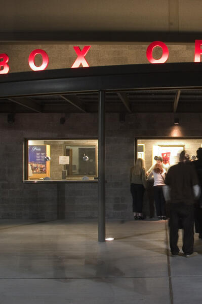 People stand in line under a portico. The signs reads "Box Office."