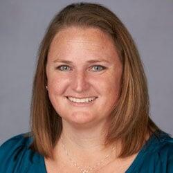 A smiling woman with auburn red hair wearing a blue blouse.