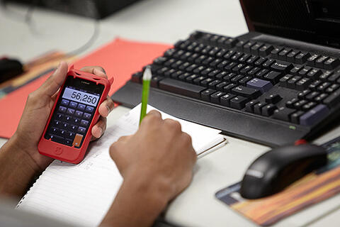 closeup of a person using a calculator with a keyboard and mouse to the side