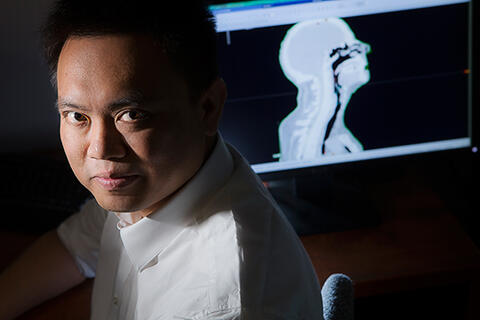 Yu Kuang poses next to computer monitor