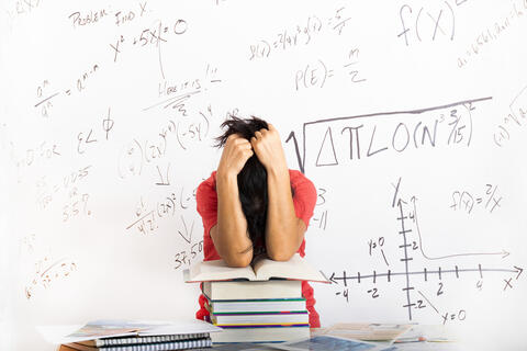 A student cradeles her head in her arms in front of a whiteboard