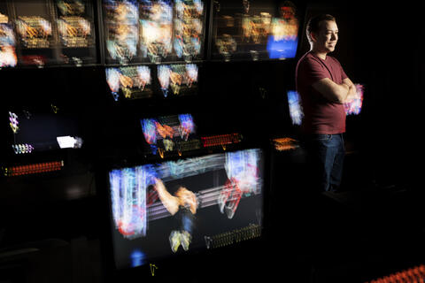 Male student standing in front of monitors with arms folded.