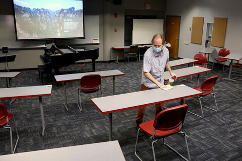 A man uses a spray bottle to disinfect a desk