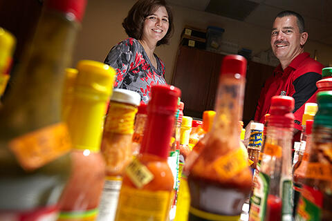 Two people looking at a variety of hot sauces on a table