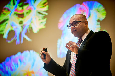 Sharang Chaudhry speaking in front of brain simulations.